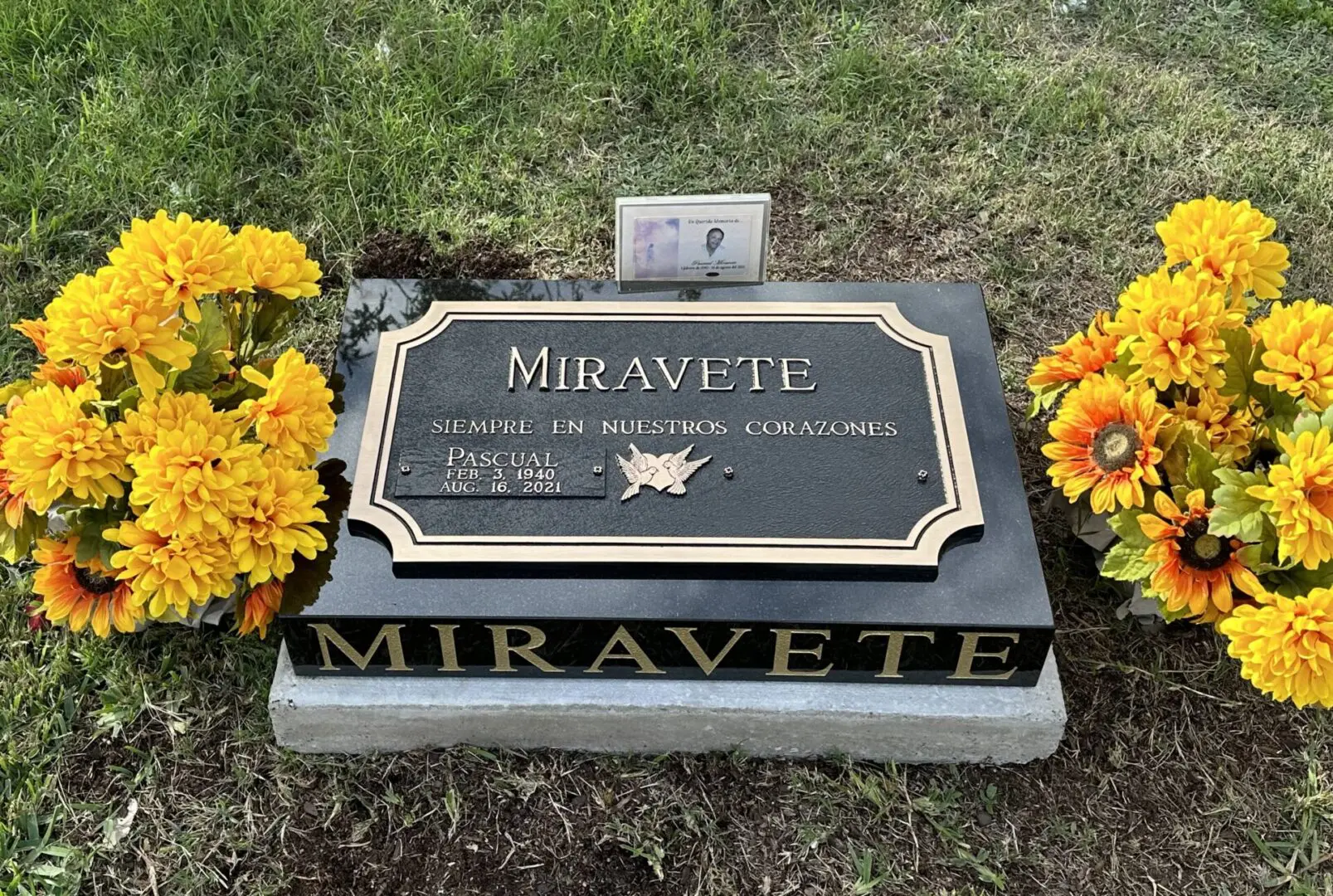 A grave stone with flowers in the grass.