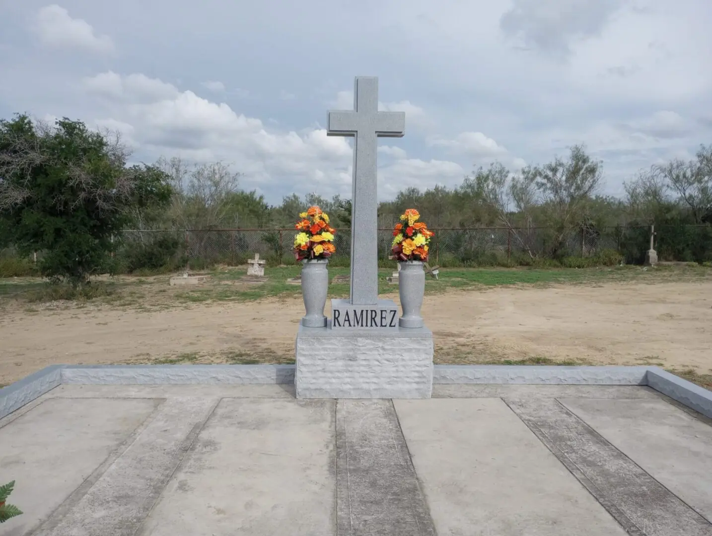 Two statues with a cross in the middle of a field.